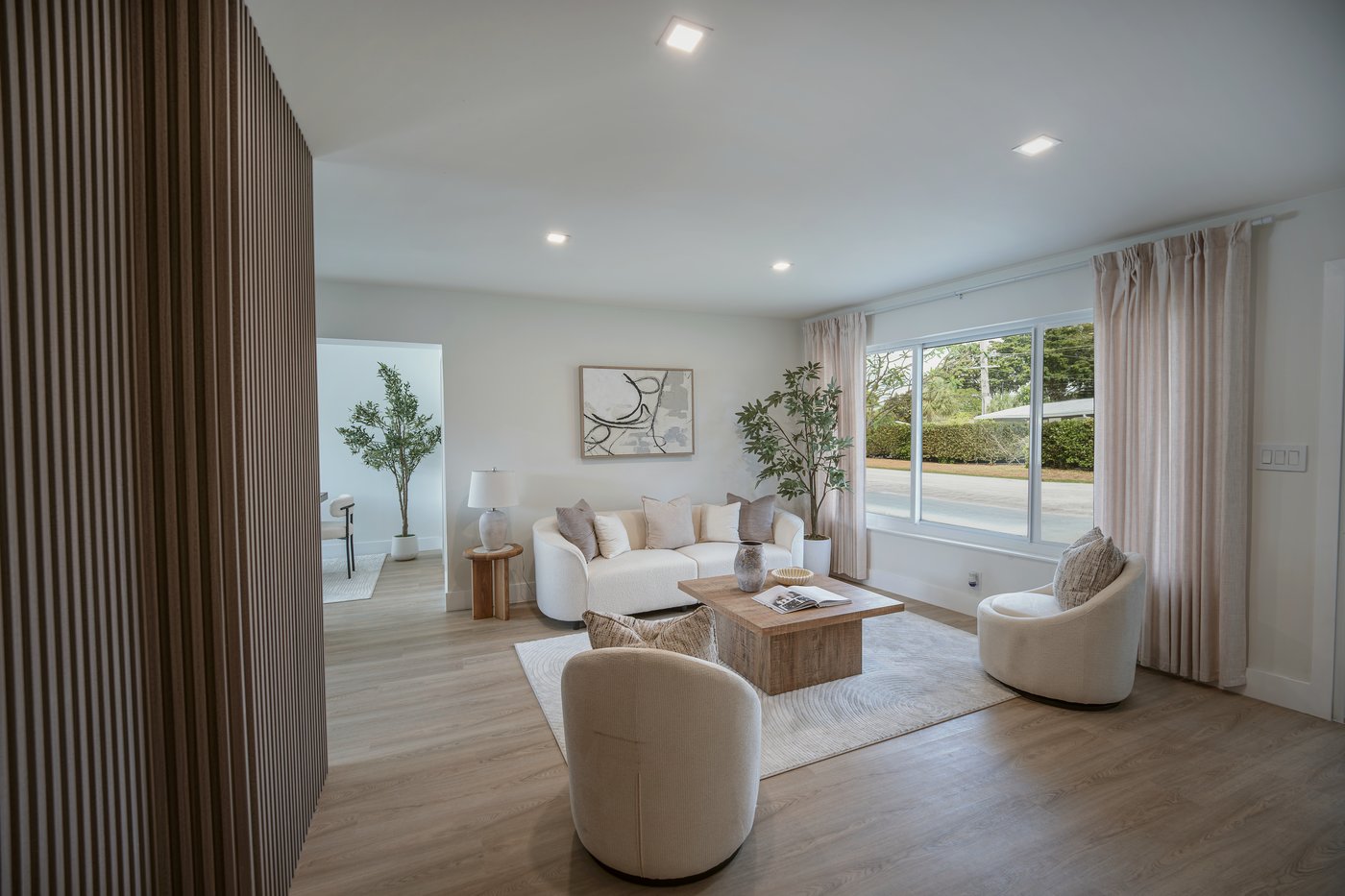 Living room with cream pleated drapery catching the afternoon light, an olive tree flanking the sofa